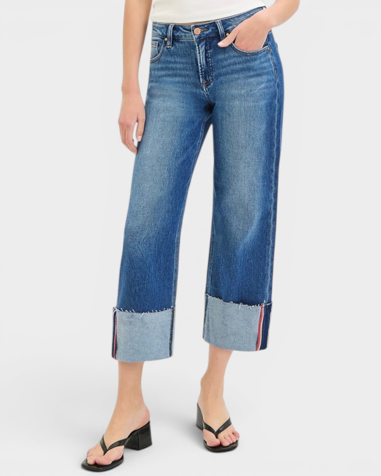 Person wearing blue jeans with cuffed hems on a white background