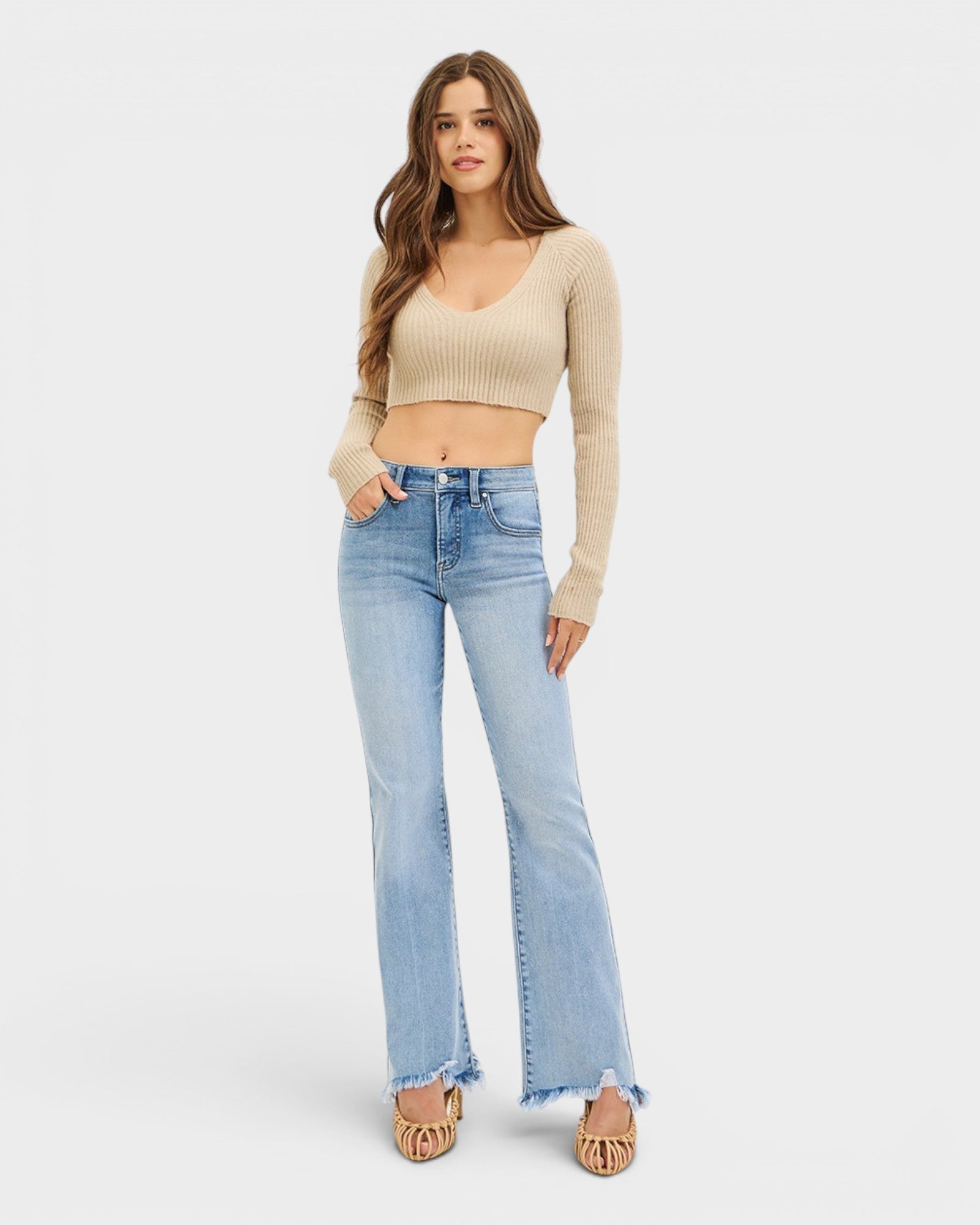 Woman wearing a beige crop top and light blue jeans on a white background