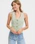 Woman wearing a light green sleeveless denim vest over a white shirt with blue jeans on a light gray background.