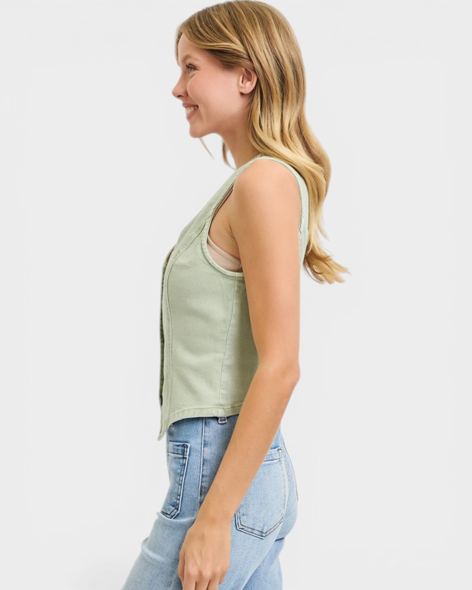 Woman wearing a light green sleeveless top and blue jeans on a white background