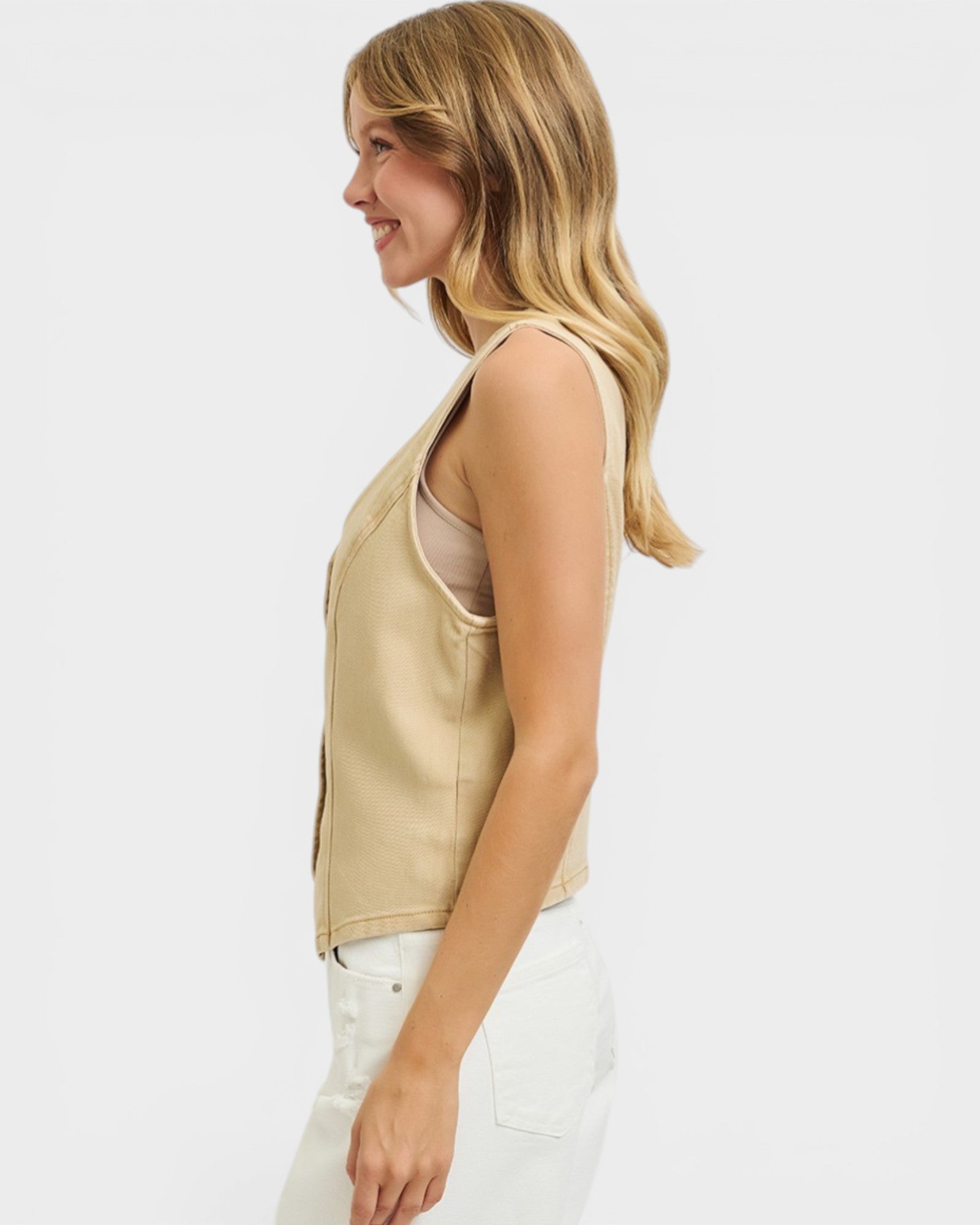 Woman wearing a beige sleeveless top and white pants on a white background