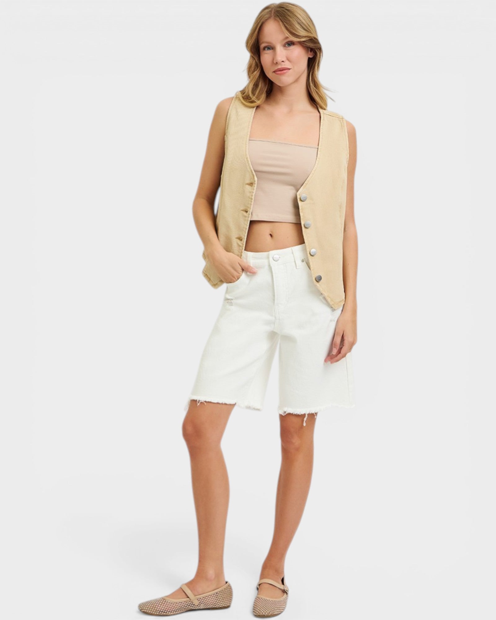 Woman wearing a beige vest, beige top, and white shorts on a white background