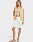 Woman wearing a beige vest, beige top, and white shorts on a white background