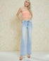 Woman wearing a strapless pink top and light blue jeans against a beige background