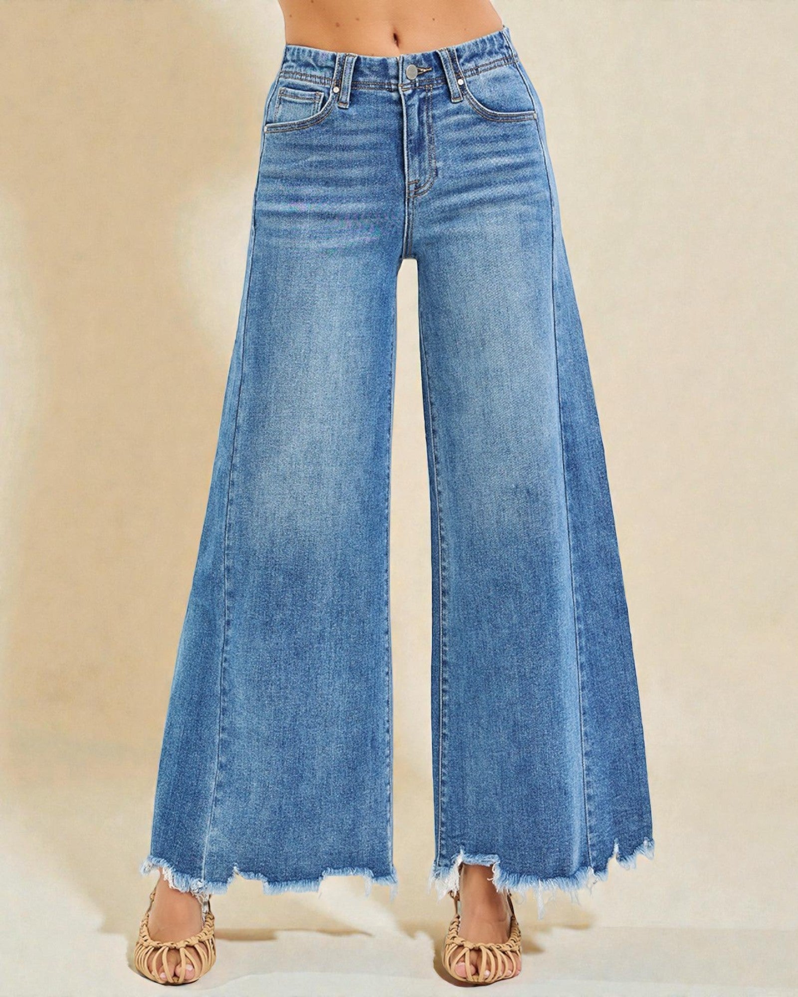 Wide-leg jeans with frayed hems on a beige background