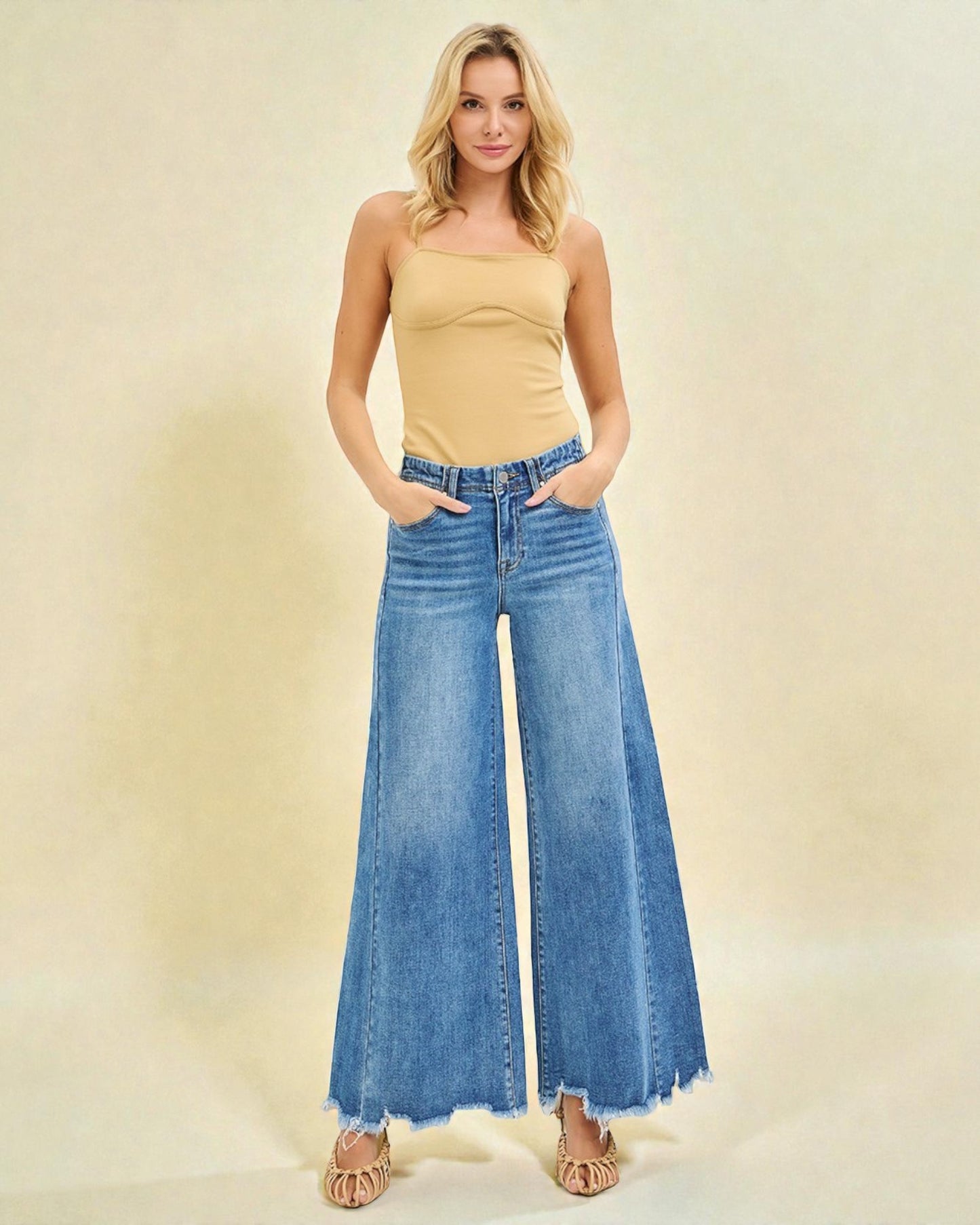 Woman wearing a yellow top and blue wide-leg jeans on a beige background