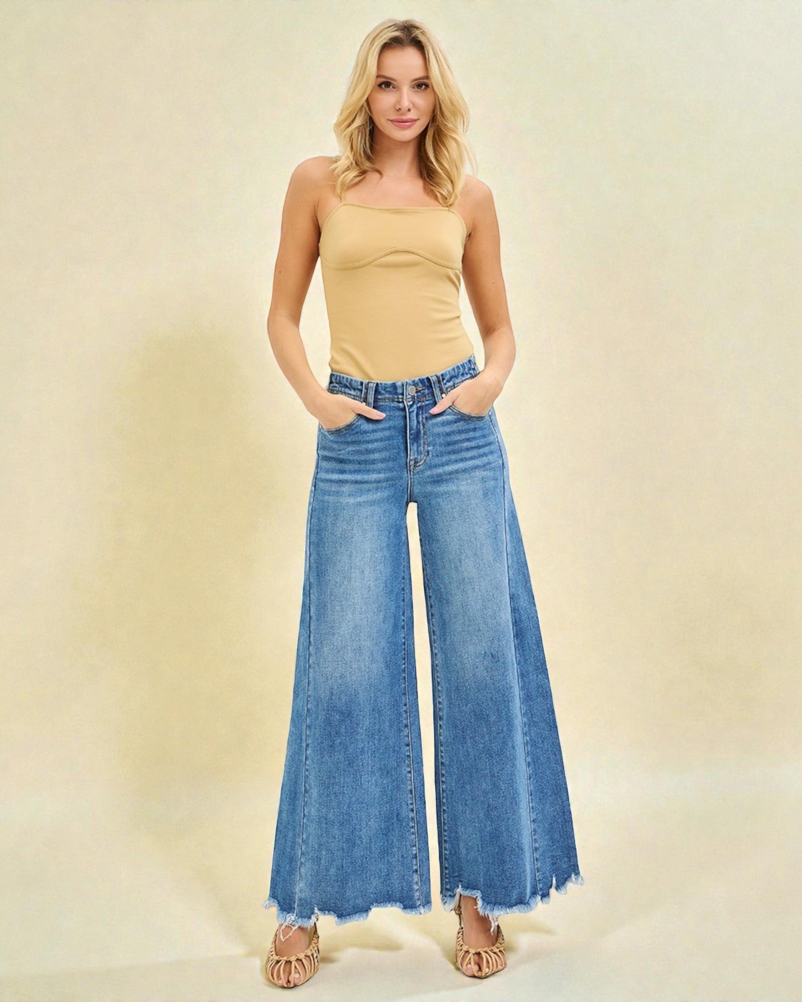 Woman wearing a yellow top and blue wide-leg jeans on a beige background