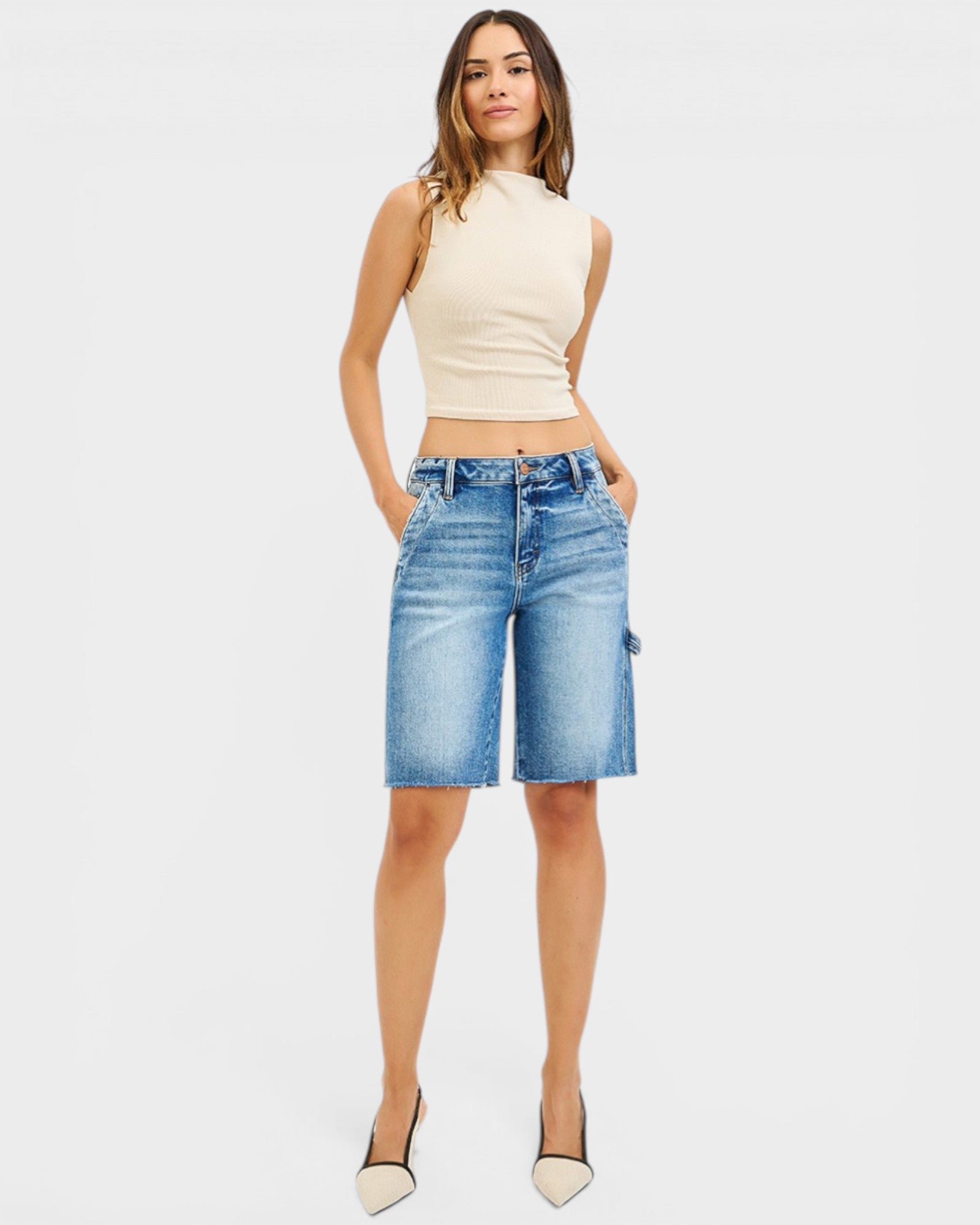 Woman wearing a beige sleeveless top and blue denim shorts on a white background