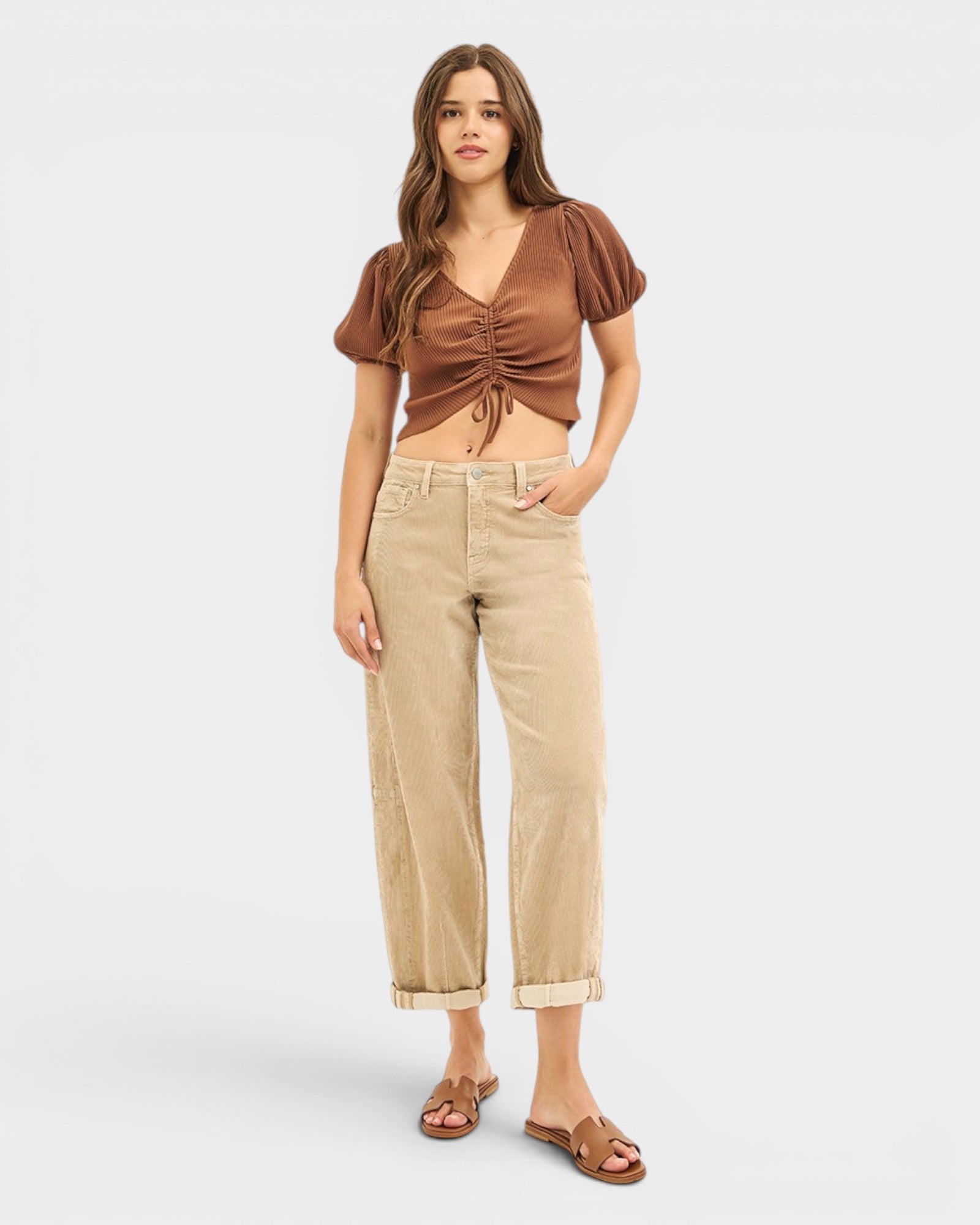 Woman wearing a brown ruched top and beige pants on a white background