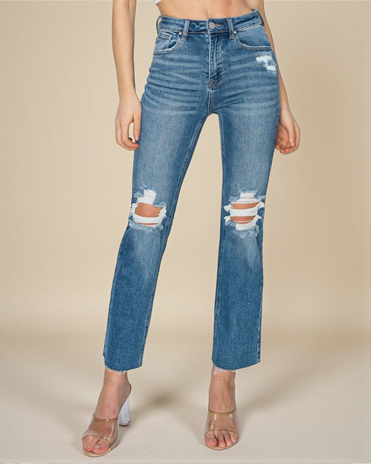 Blue distressed jeans worn by a person on a beige background