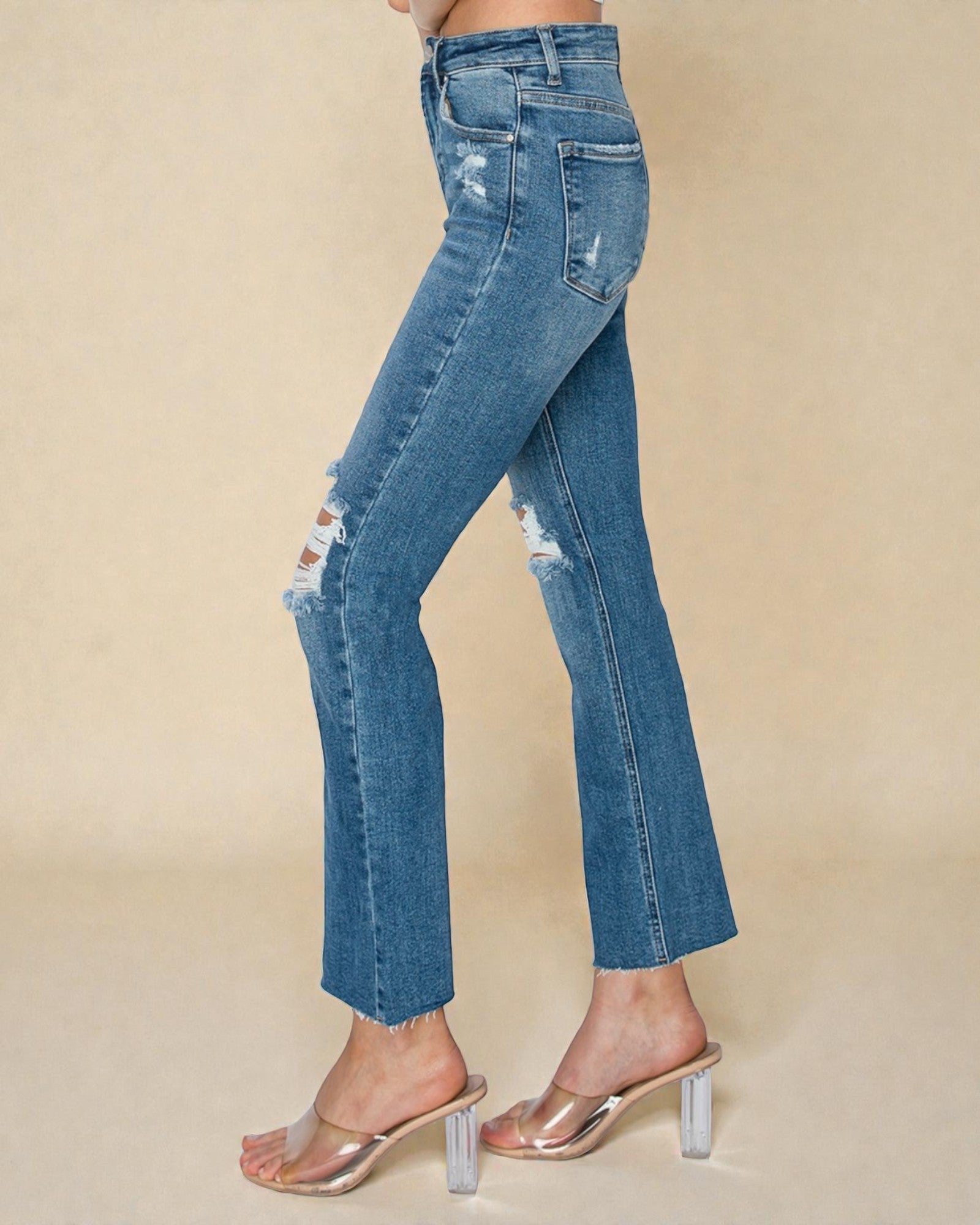 Blue distressed jeans worn by a person on a beige background