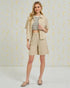 Woman wearing a beige jacket, striped top, and shorts against a light background