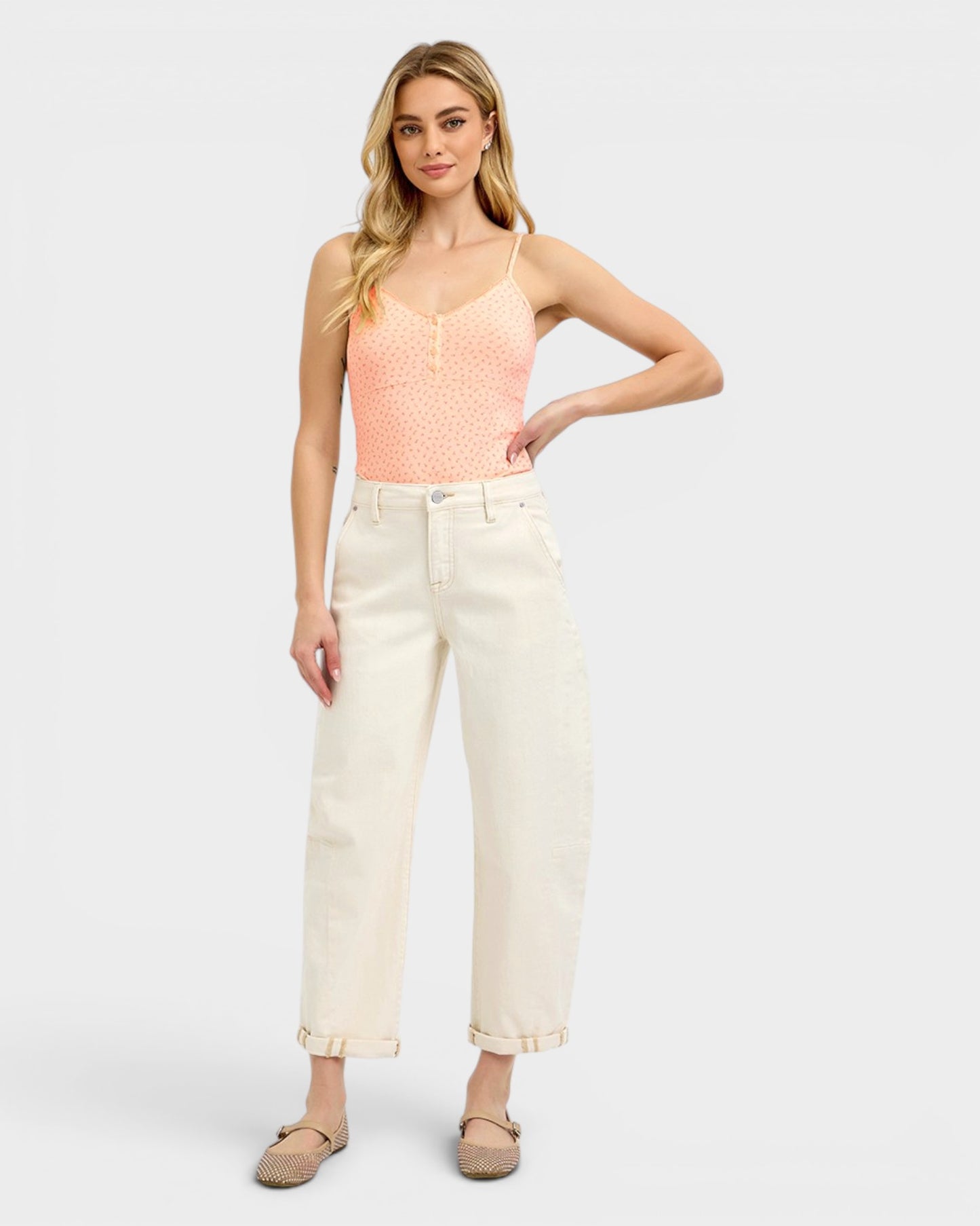 Woman wearing a pink top and white pants on a light gray background