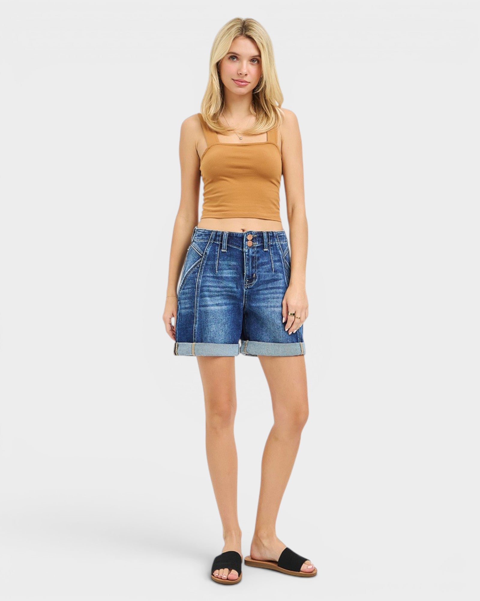 Woman wearing a tan tank top and blue denim shorts on a white background