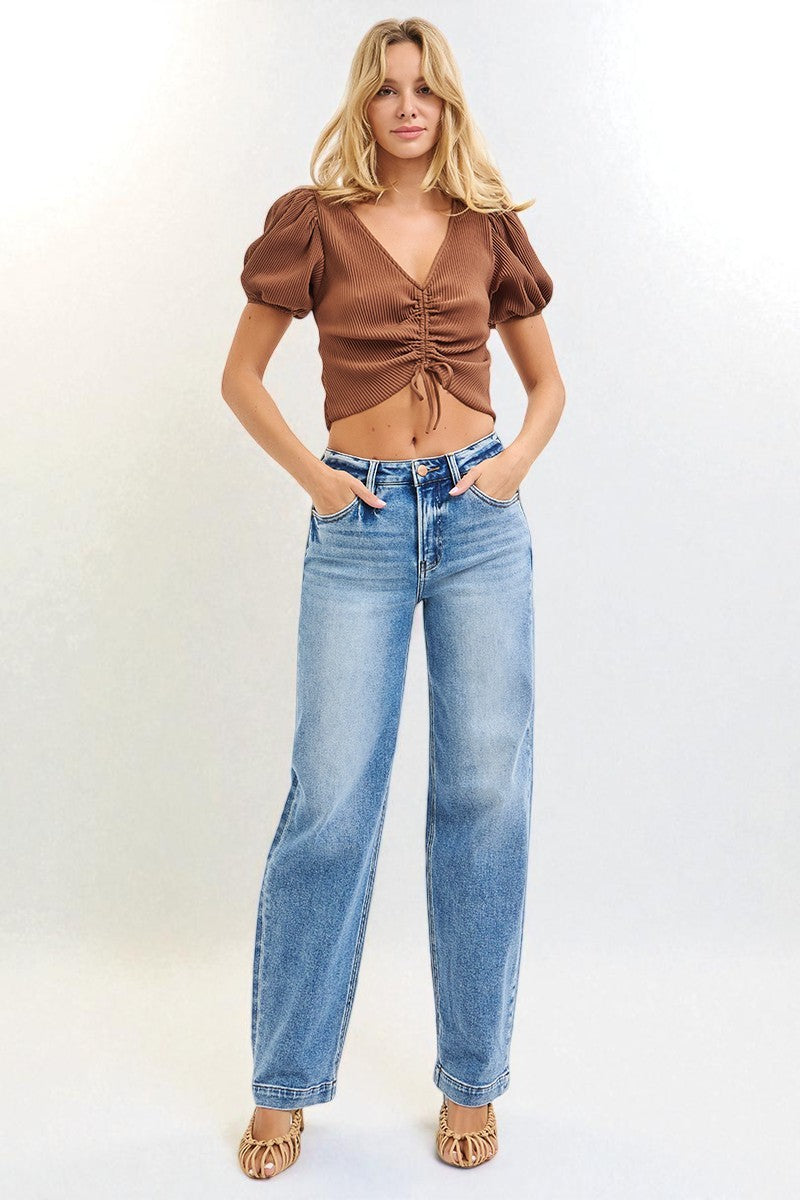 Woman wearing a brown top and blue jeans against a white background