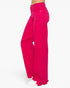 Bright pink wide-leg denim jeans shown on a model from the side, featuring raw, frayed hems and white sneakers against a plain white background.