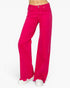 Bright pink wide-leg jeans with raw, frayed hems, shown on a model from the waist down wearing white sneakers against a plain white background.