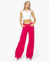 A woman modeling bright fuchsia wide-leg jeans with a white cropped tank top featuring a chest cutout, standing against a plain white studio background.