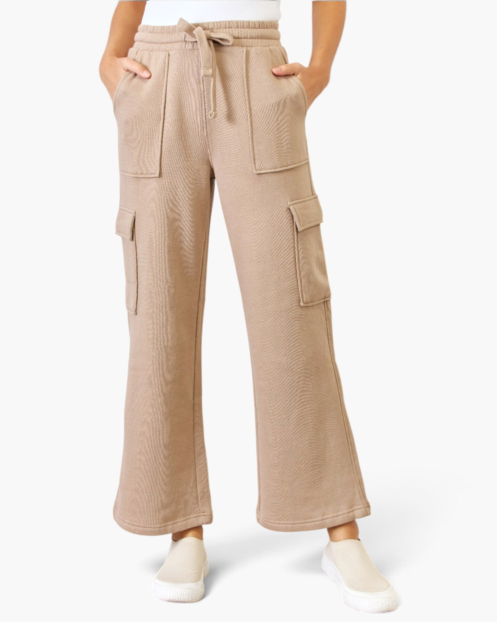 A person wearing beige wide-leg cargo pants with a textured wavy pattern, a drawstring waist, and side cargo pockets, paired with white socks and a white top against a light gray studio background.