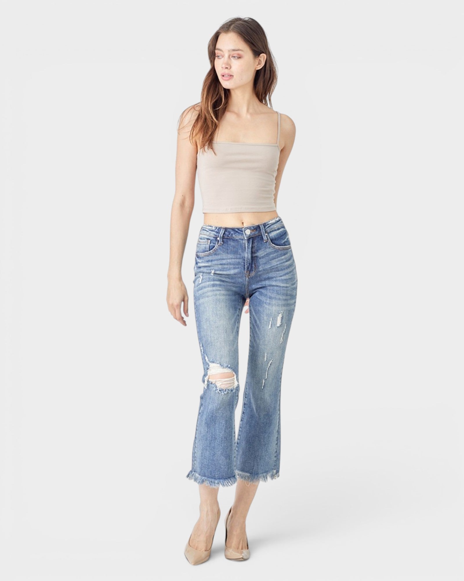 Woman wearing a beige strapless top and distressed blue jeans on a white background
