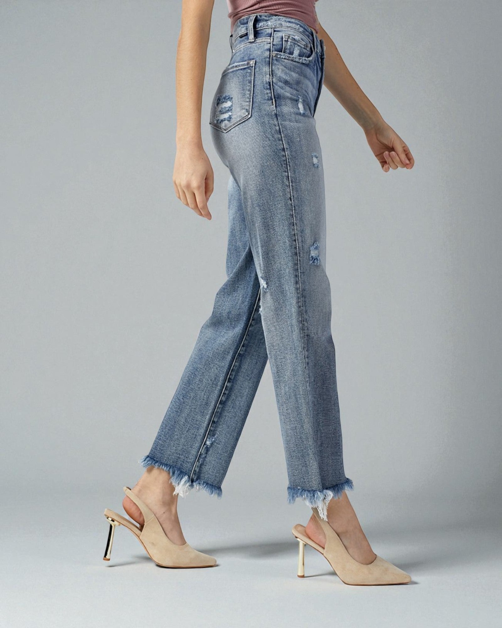 Person wearing blue jeans and beige high-heeled shoes on a gray background