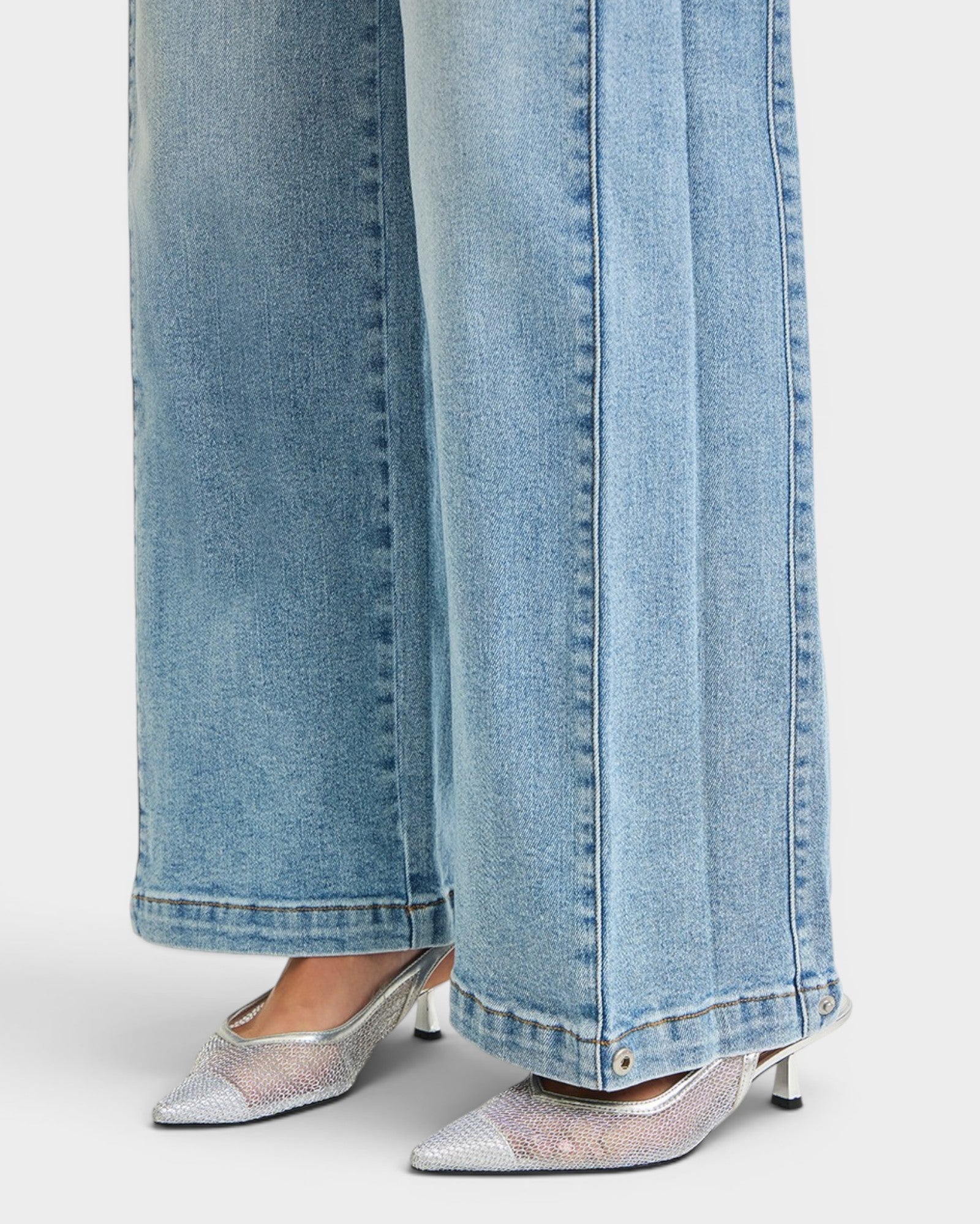 Close-up of light blue jeans with a person wearing silver shoes on a white background