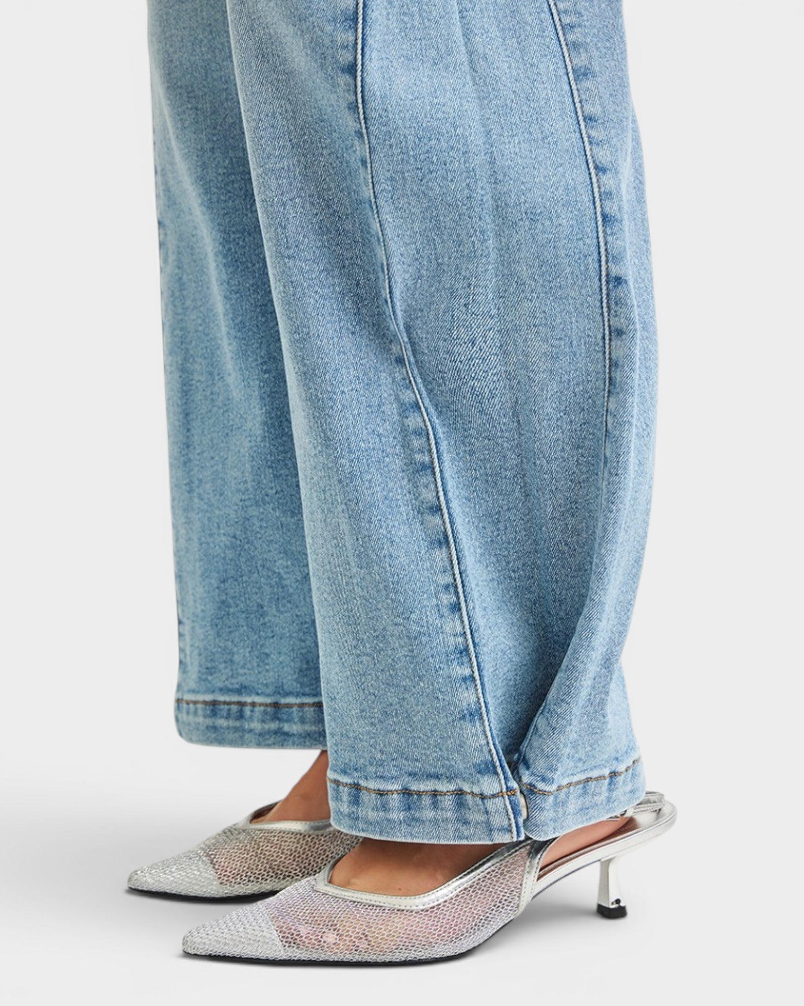 Close-up of light blue jeans and silver high-heeled shoes on a white background