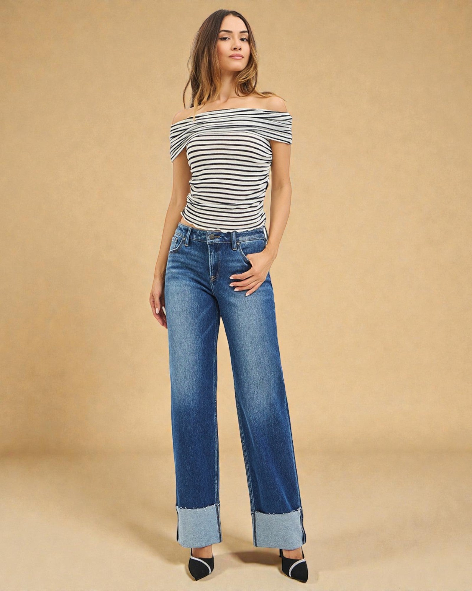 Woman wearing a striped off-shoulder top and blue jeans against a beige background