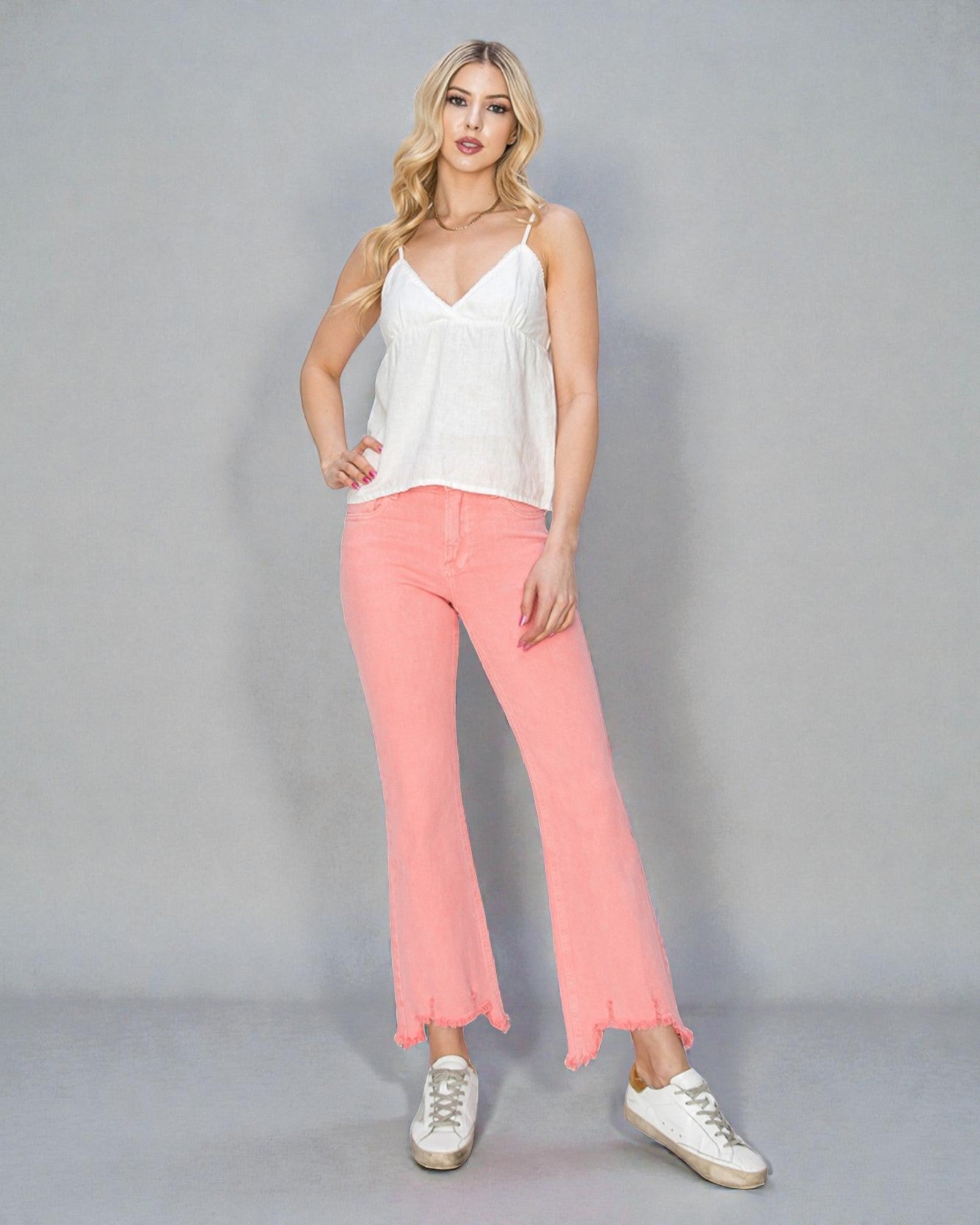 Woman wearing a white top and pink pants against a gray background