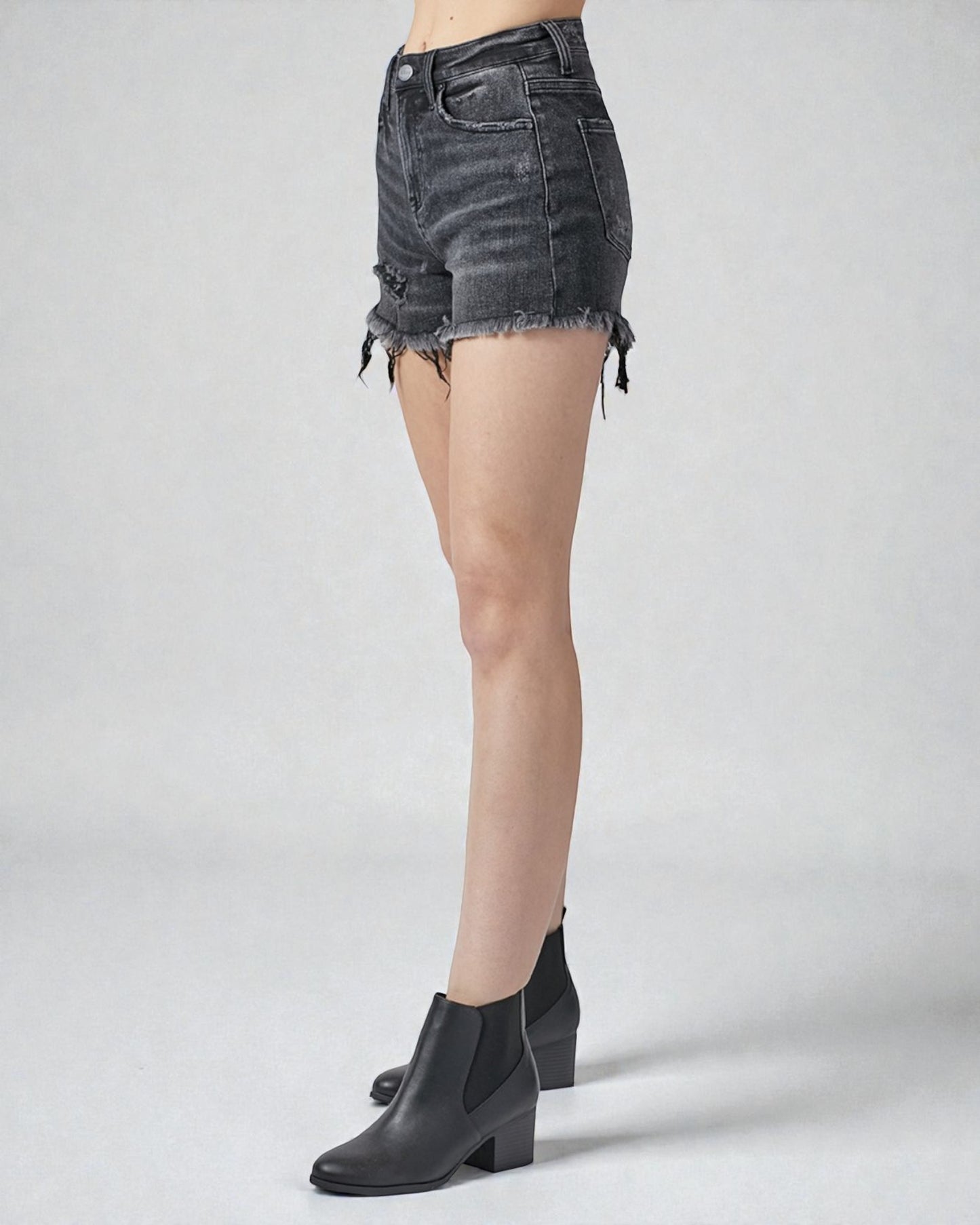 Person wearing black denim shorts and black boots on a white background