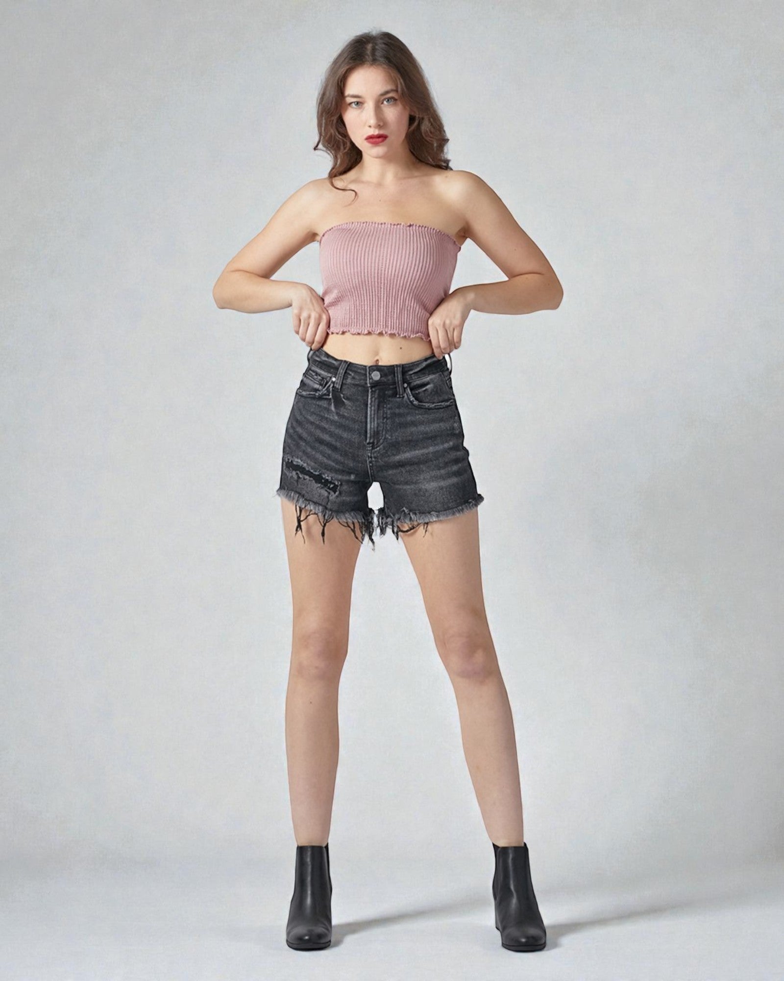 Woman wearing a pink strapless top and black denim shorts on a plain background