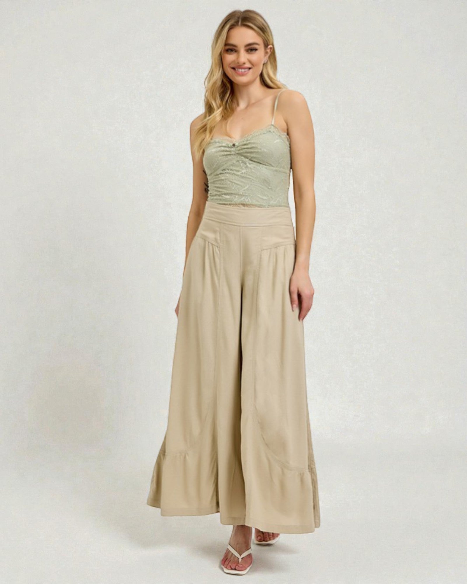 Woman wearing a green top and beige wide-leg pants on a white background