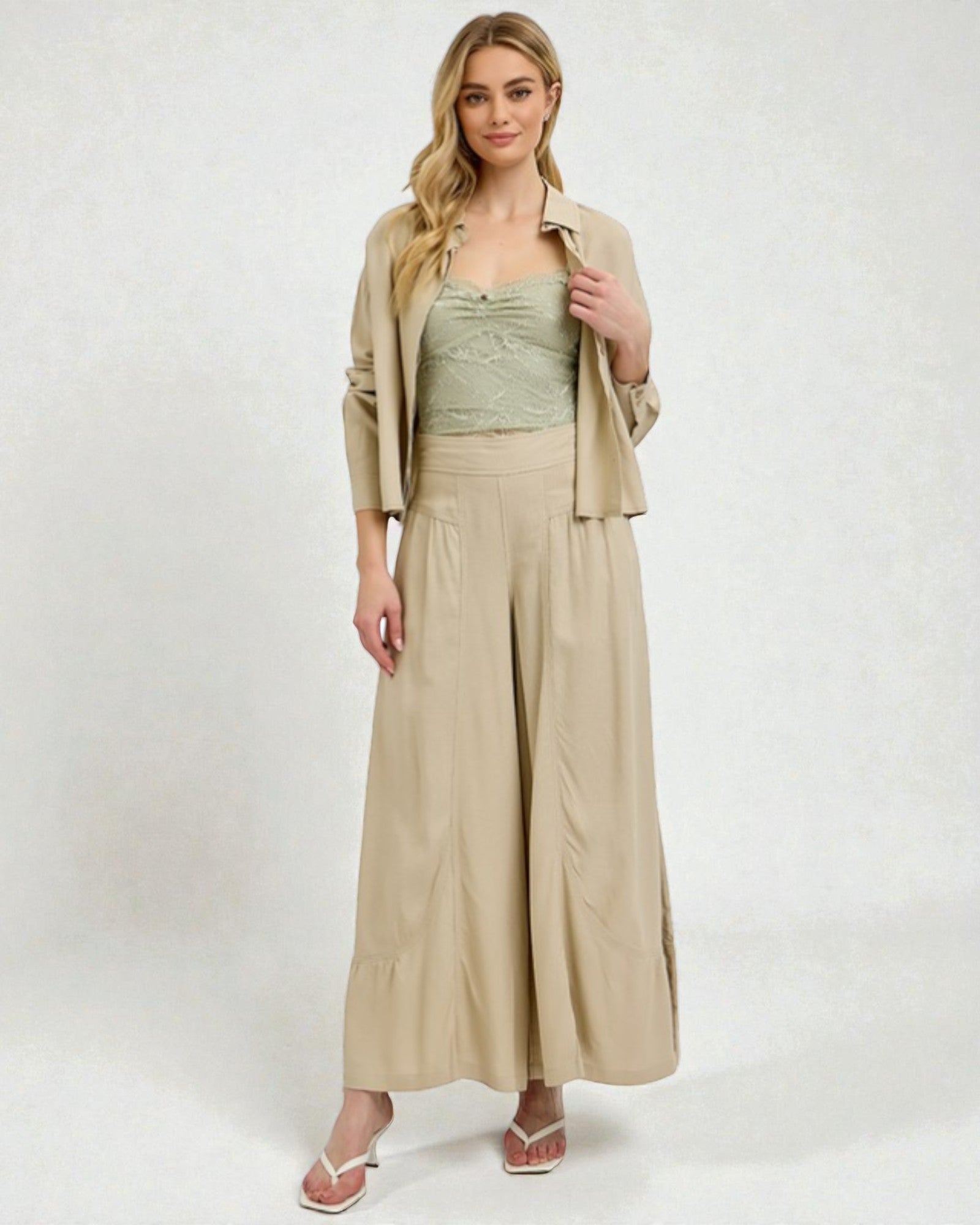 Woman wearing a beige jacket, green top, and wide-leg pants on a white background