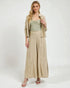 Woman wearing a beige jacket, green top, and wide-leg pants on a white background