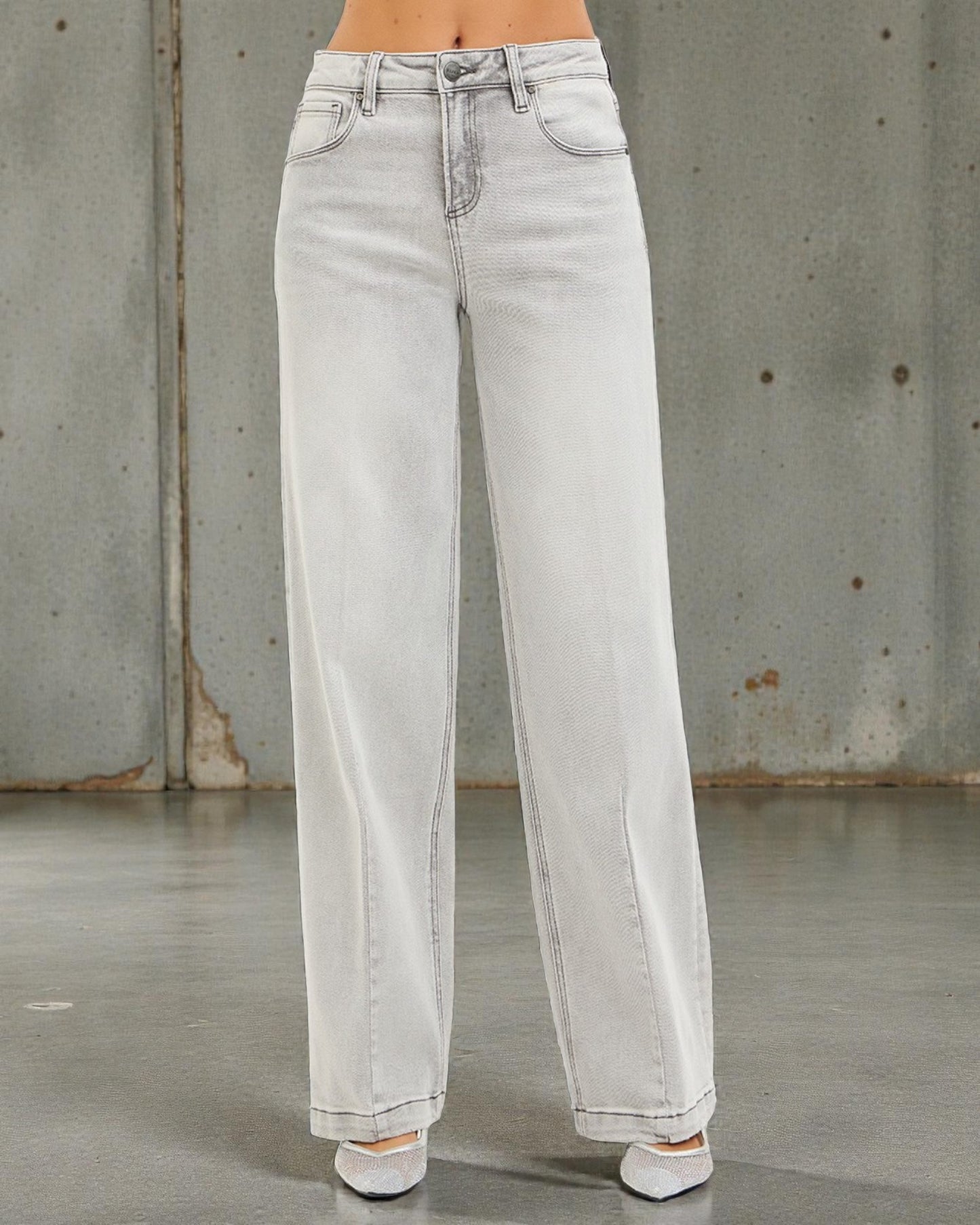 Light blue jeans worn by a person against a gray concrete wall.