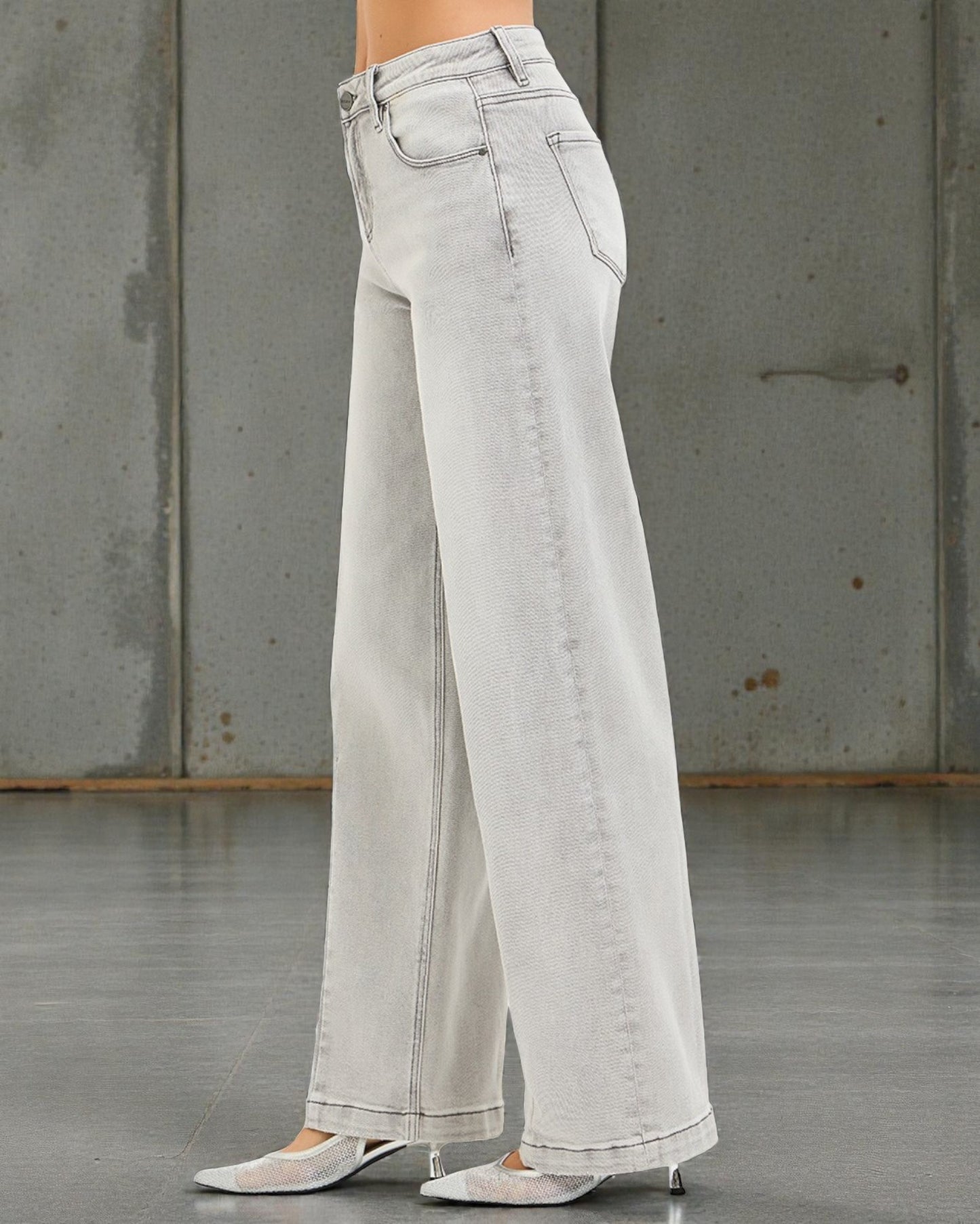 Light gray wide-leg jeans worn by a person against a concrete wall.