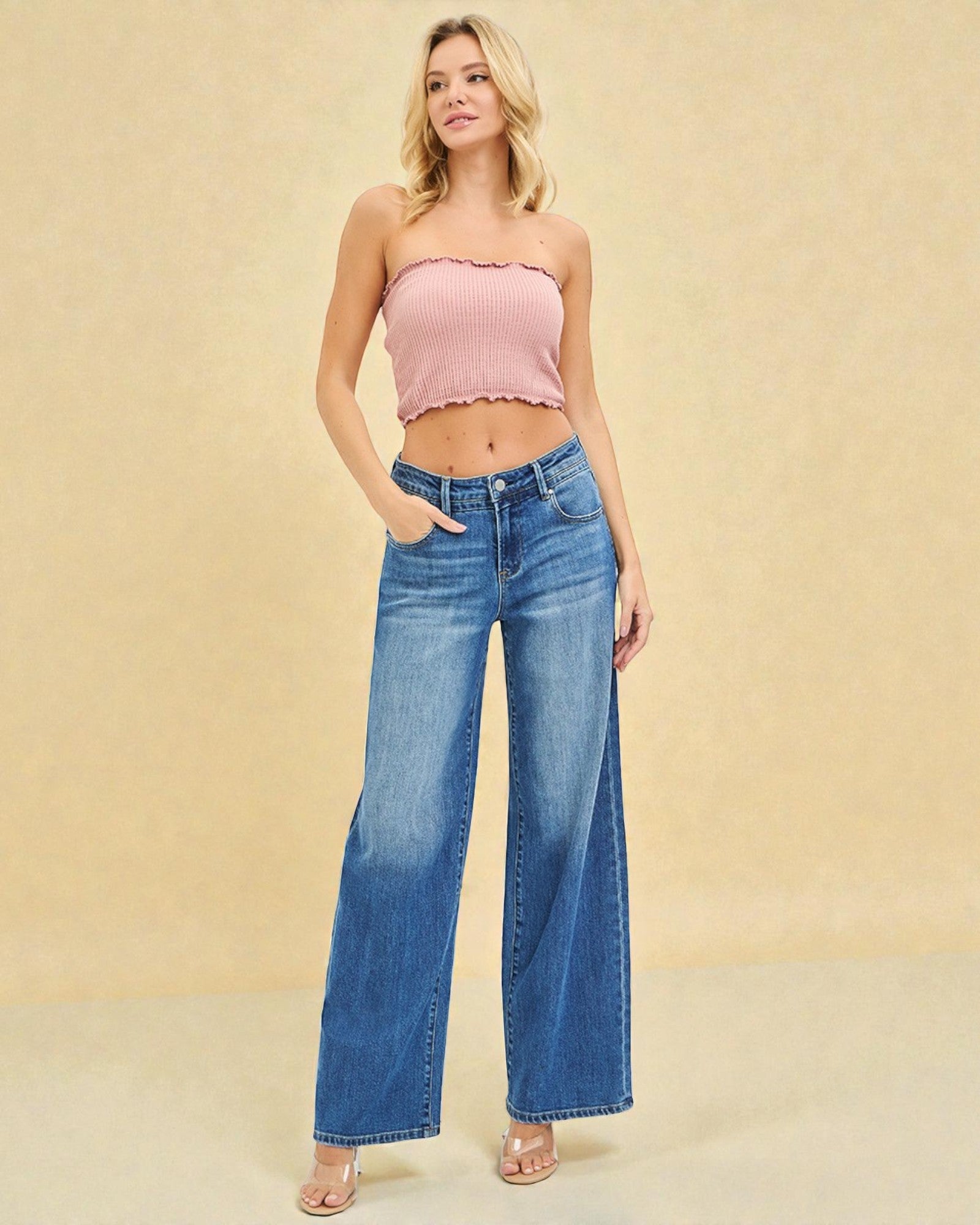 Woman wearing a pink strapless top and blue jeans against a beige background