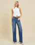 Woman wearing a white sleeveless top and blue jeans on a beige background