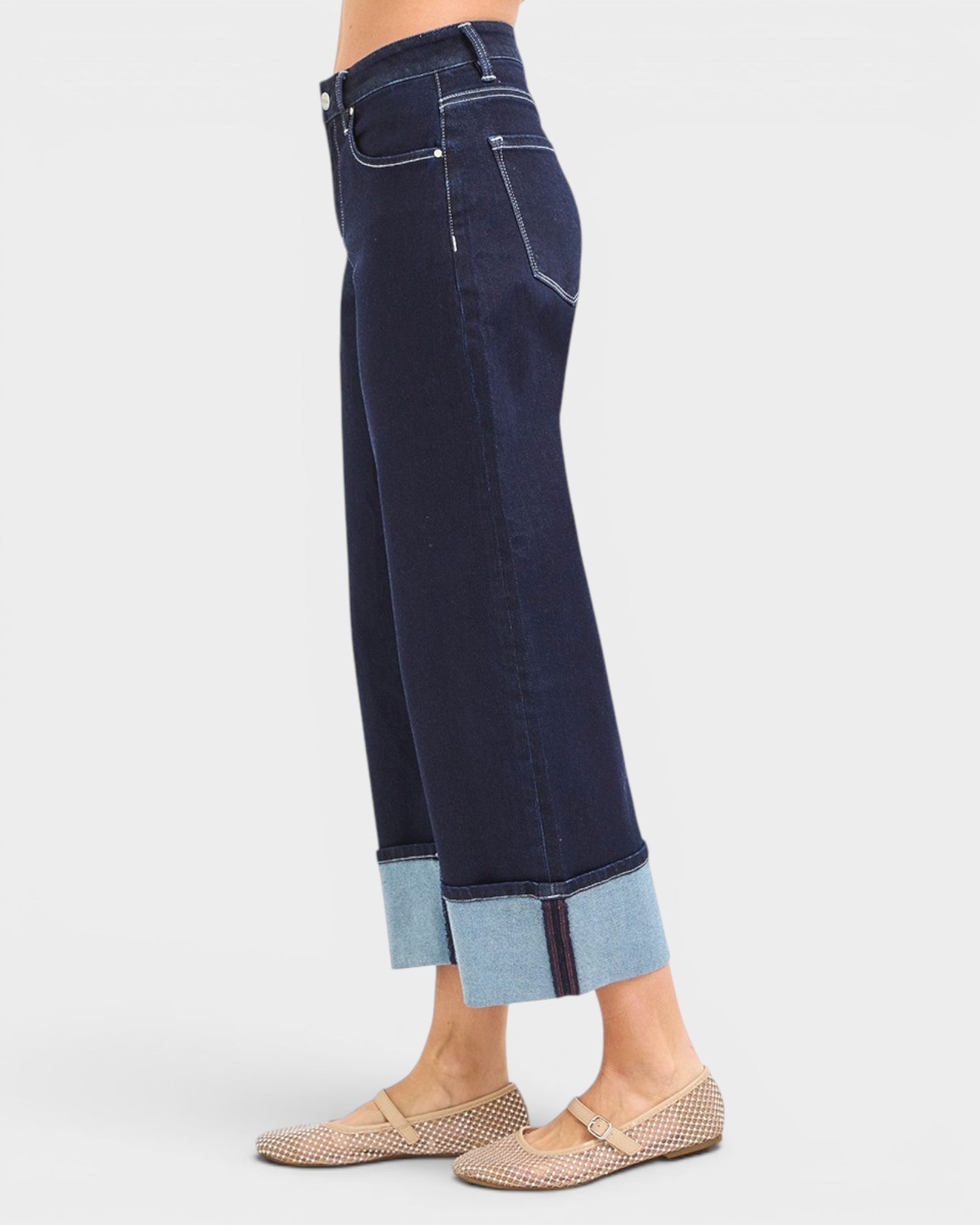 Dark blue jeans with light blue cuffs worn by a person on a white background