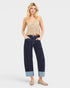 Woman wearing a beige tank top and dark blue jeans on a white background