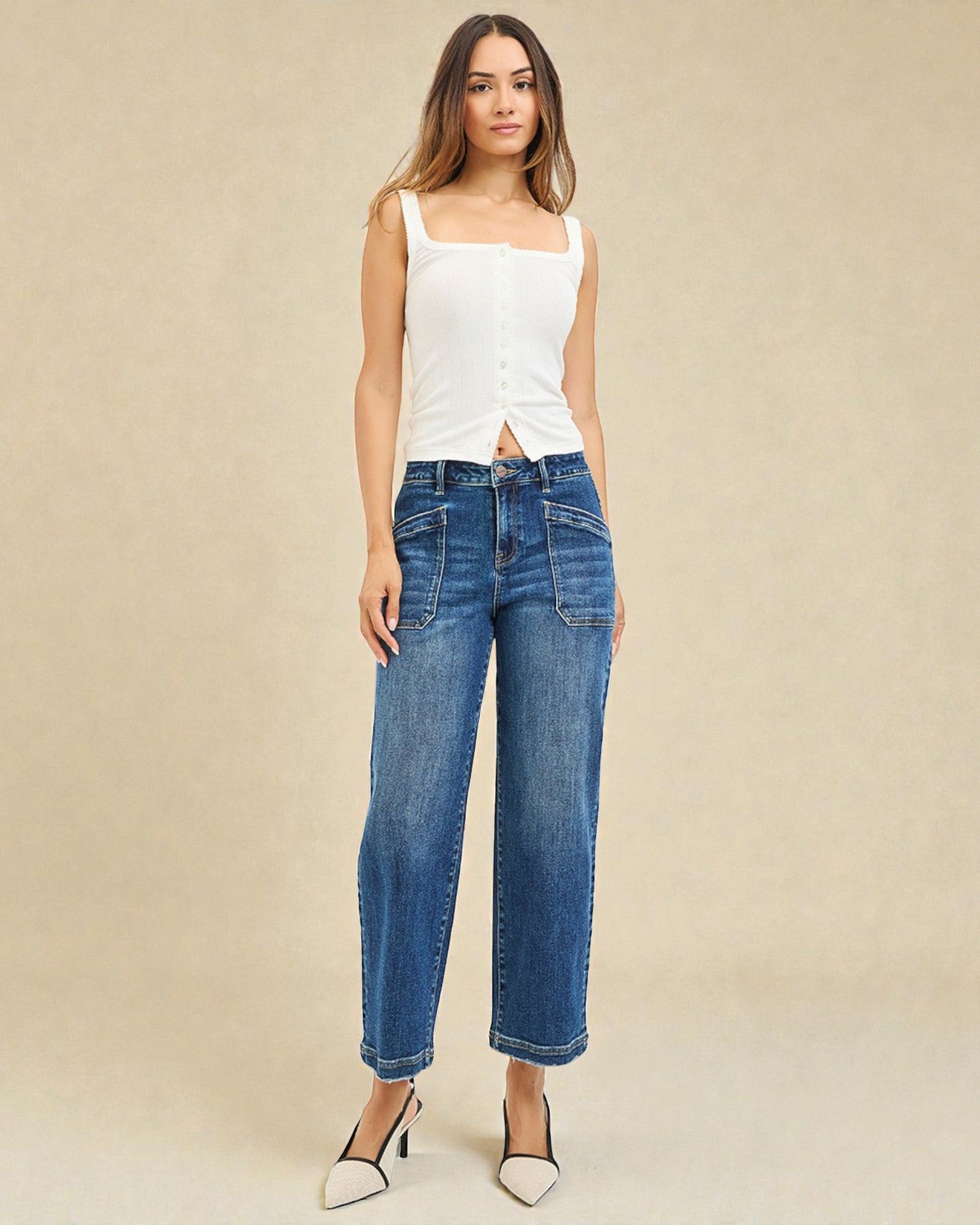 Woman wearing a white sleeveless top and blue jeans against a beige background