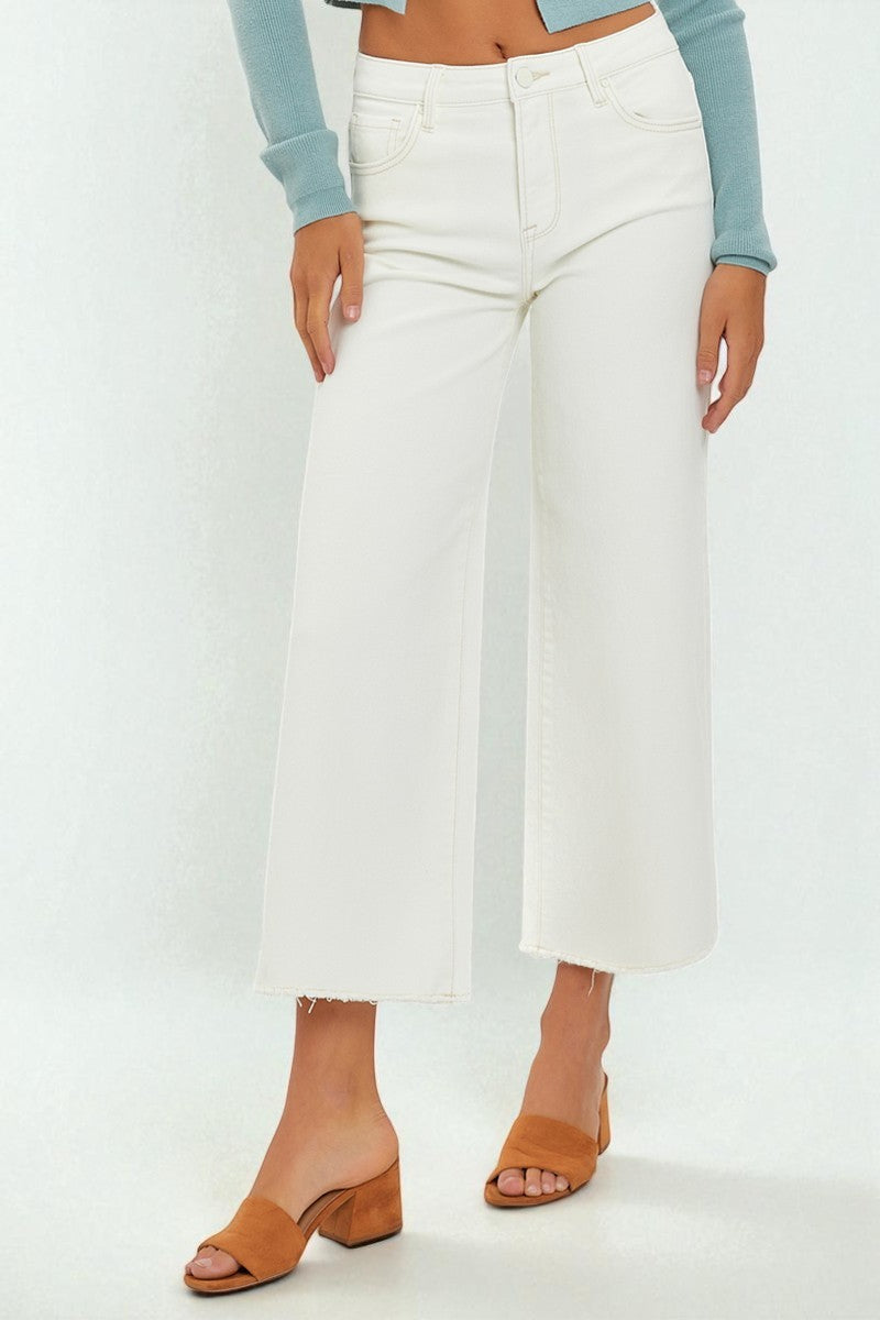 Person wearing white wide-leg pants with a light blue top and brown sandals on a white background