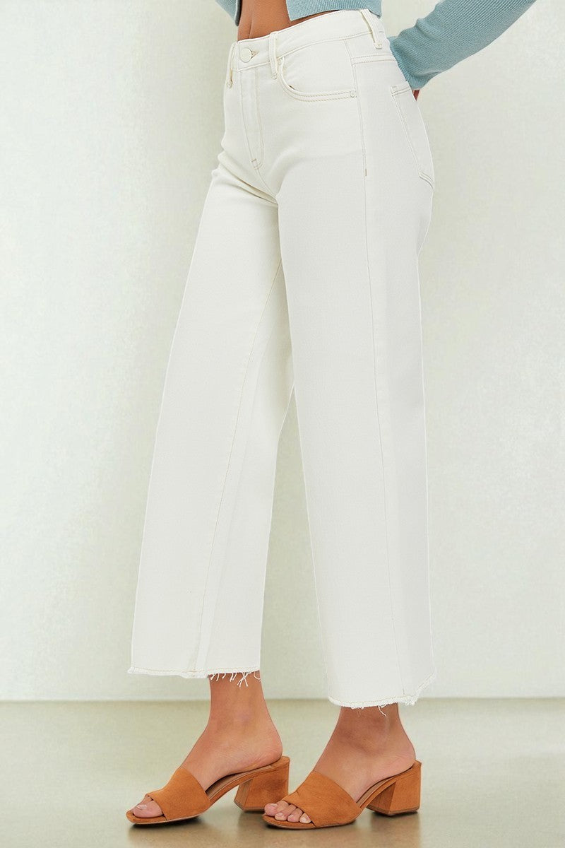 Person wearing white wide-leg jeans and brown sandals on a plain background