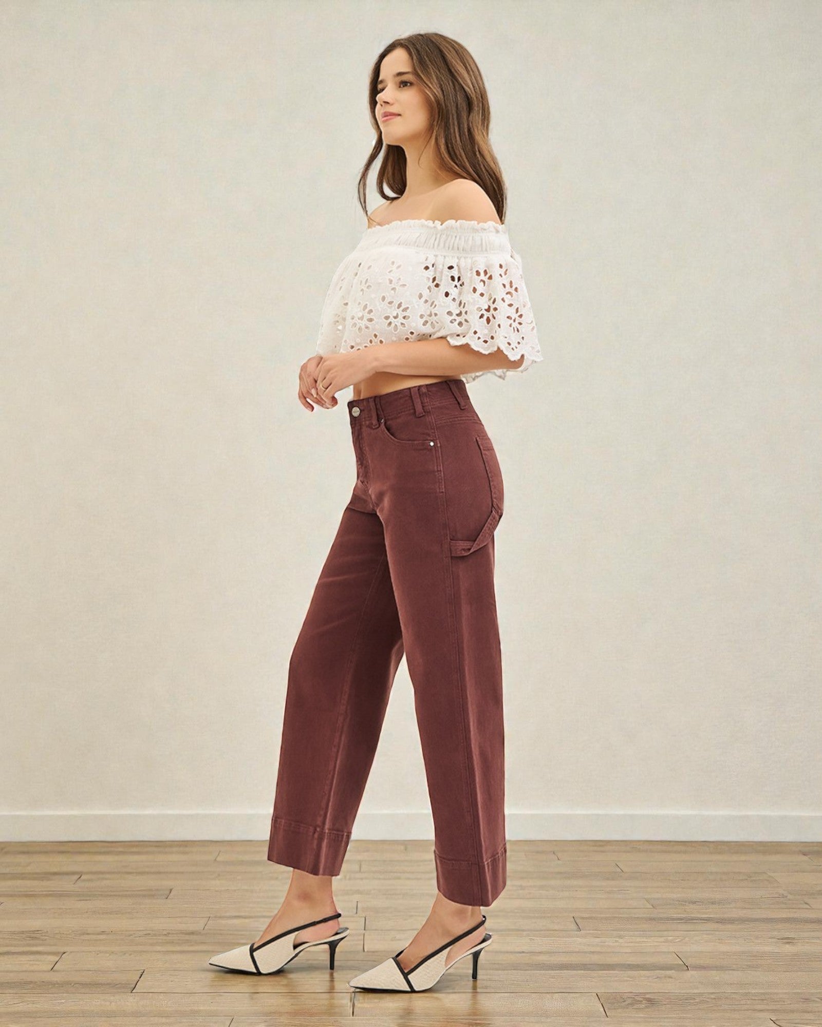 Woman wearing a white off-shoulder top and maroon pants against a plain background