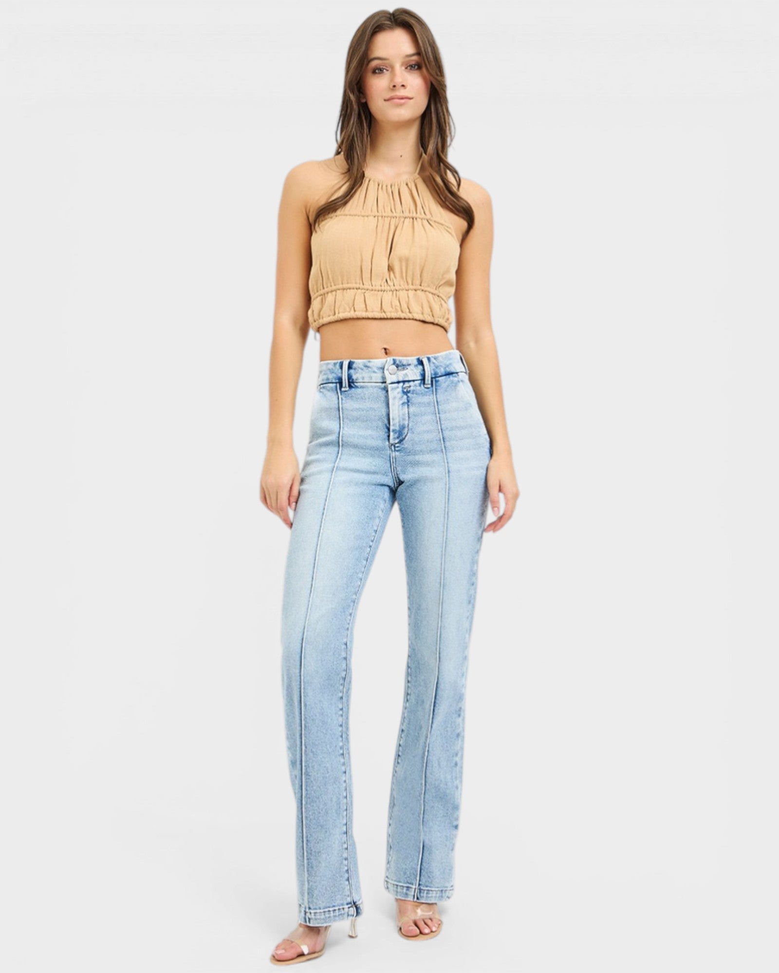 Woman wearing a beige top and light blue jeans on a white background
