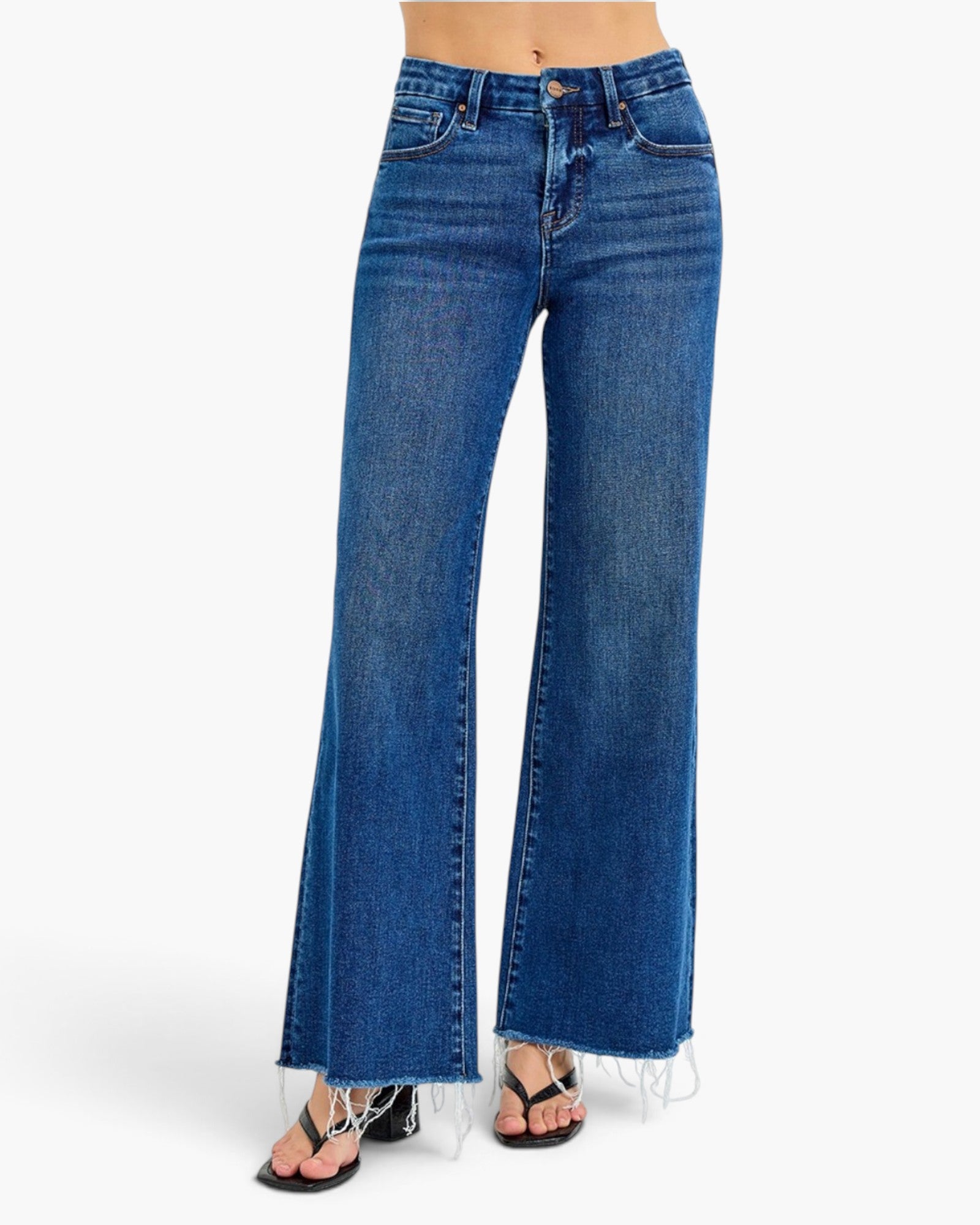 A model is wearing a pair of high-waisted, wide-leg blue denim jeans with a raw frayed hem, styled with black strappy sandals against a plain white background.