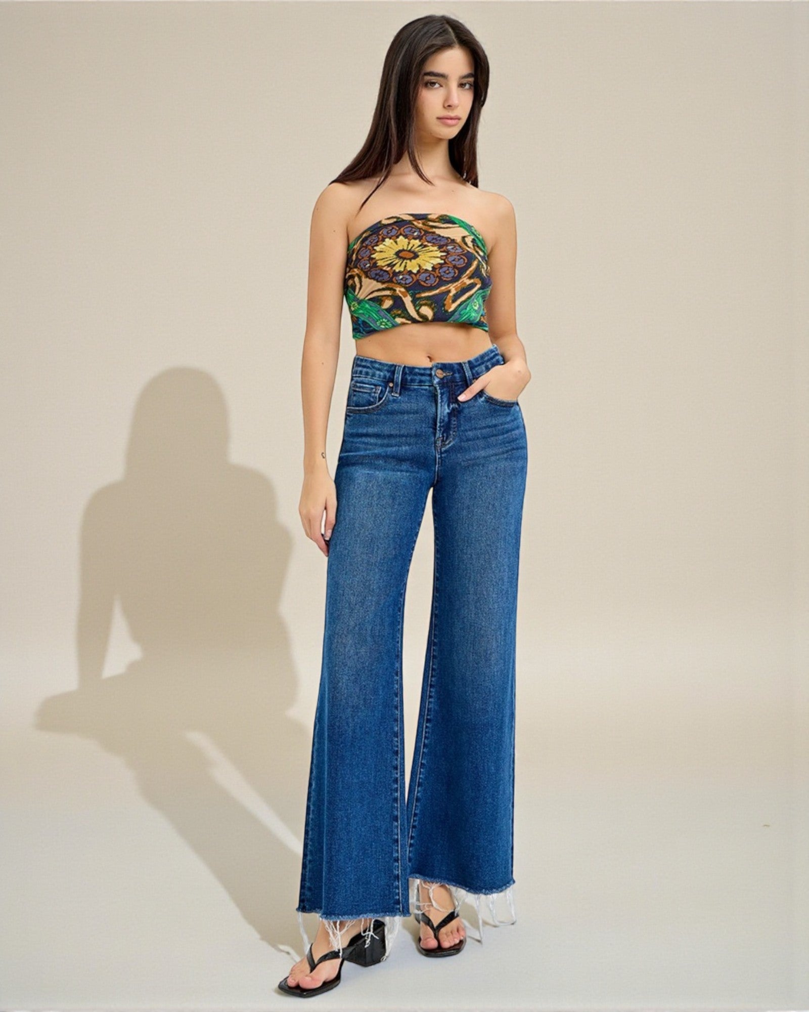 Woman wearing a floral top and blue jeans against a plain background