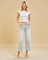 Woman wearing a white crop top and light blue jeans against a beige background