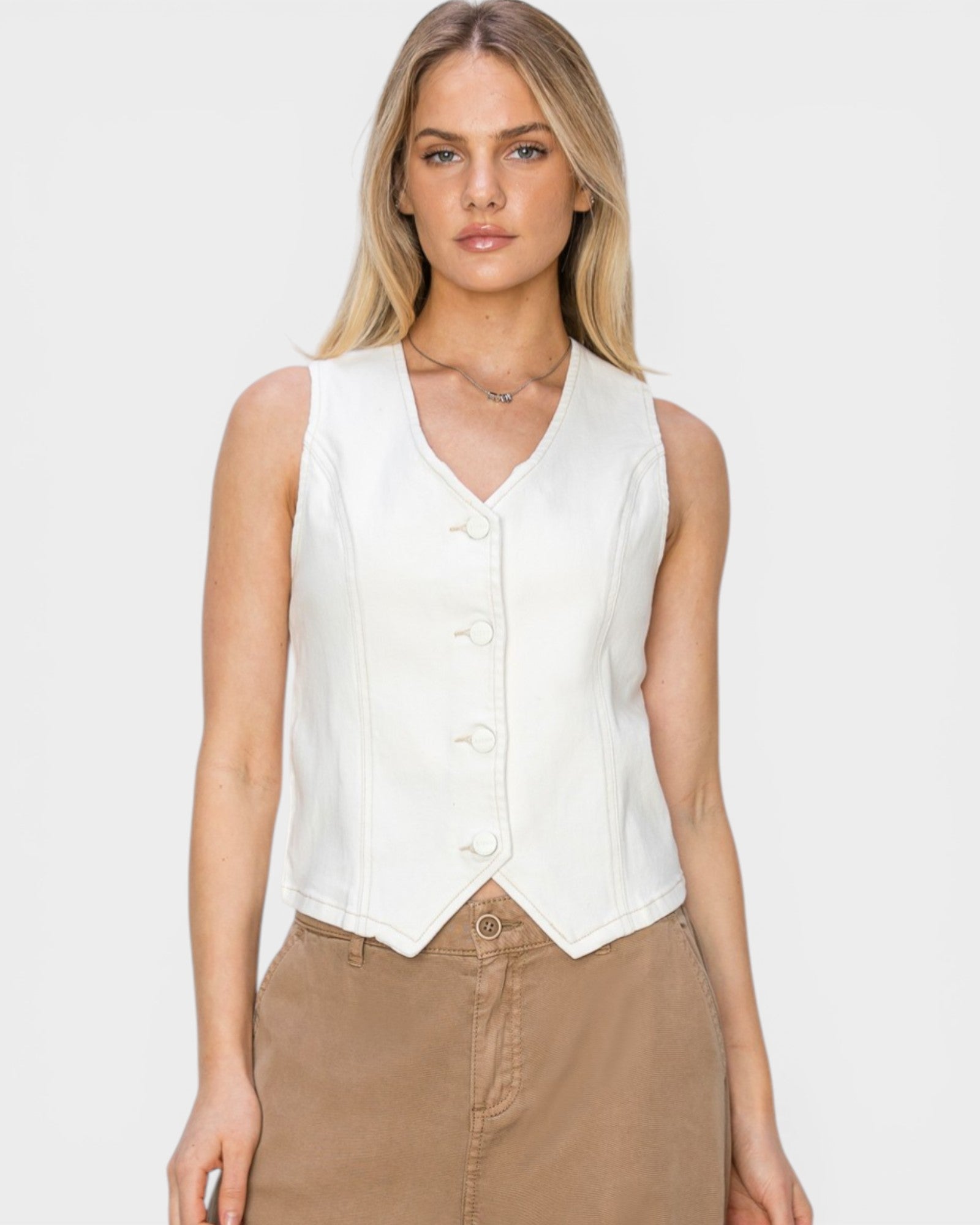 Woman wearing a white sleeveless blouse and brown pants on a plain background