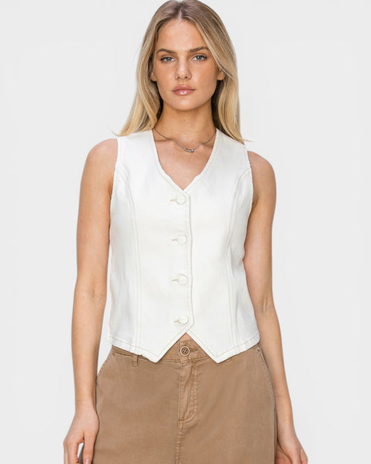 Woman wearing a white sleeveless blouse and brown pants on a plain background
